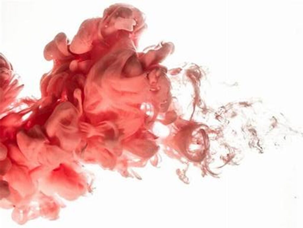 Swirling red and pink ink in water against a white background creates a cloud-like effect.