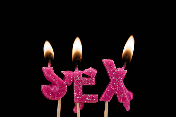 Three pink candles shaped as the word "SEX" are lit against a black background.