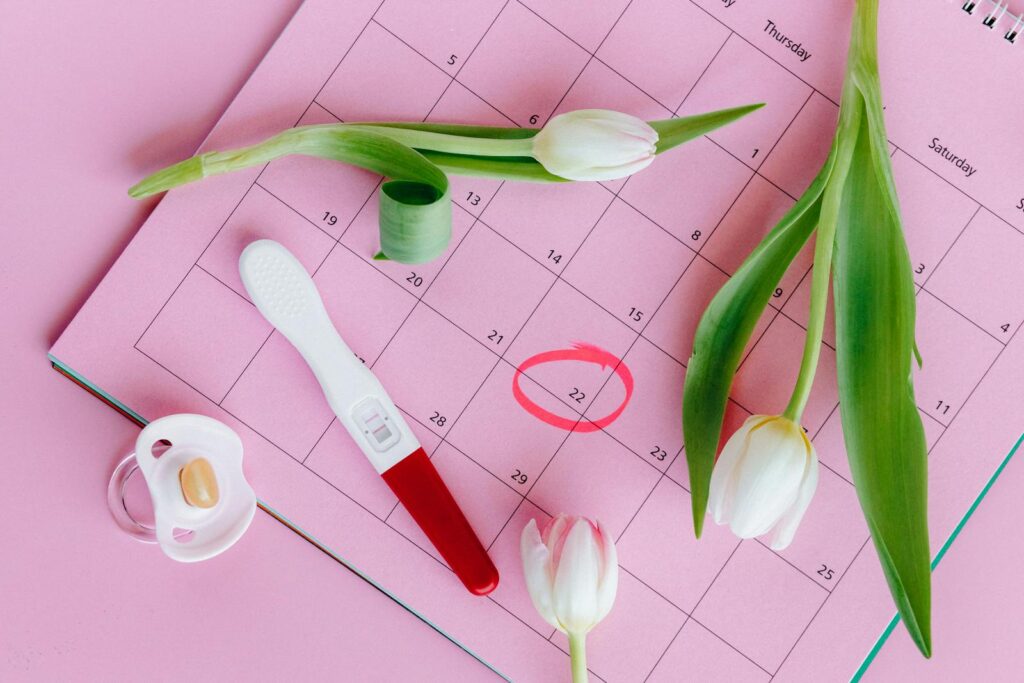 Test de grossesse sur un calendrier rose avec des tulipes, symbolisant la fertilité et les nouveaux départs.